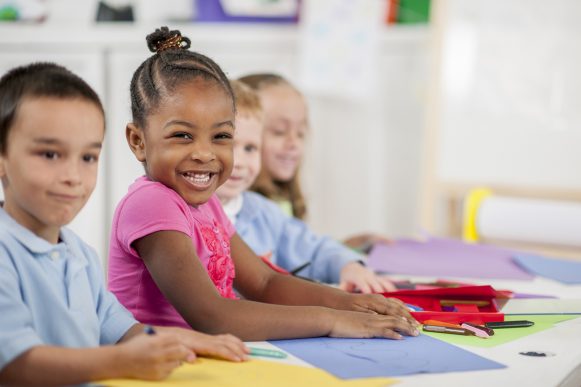 A multi-ethnic group of elementary age children are coloring on construction paper and making an art project in class.